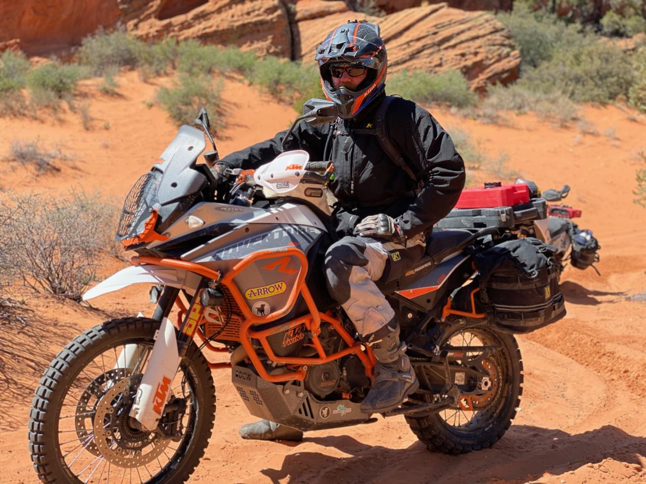 A rider on a KTM adventure bike on a red-rock trail